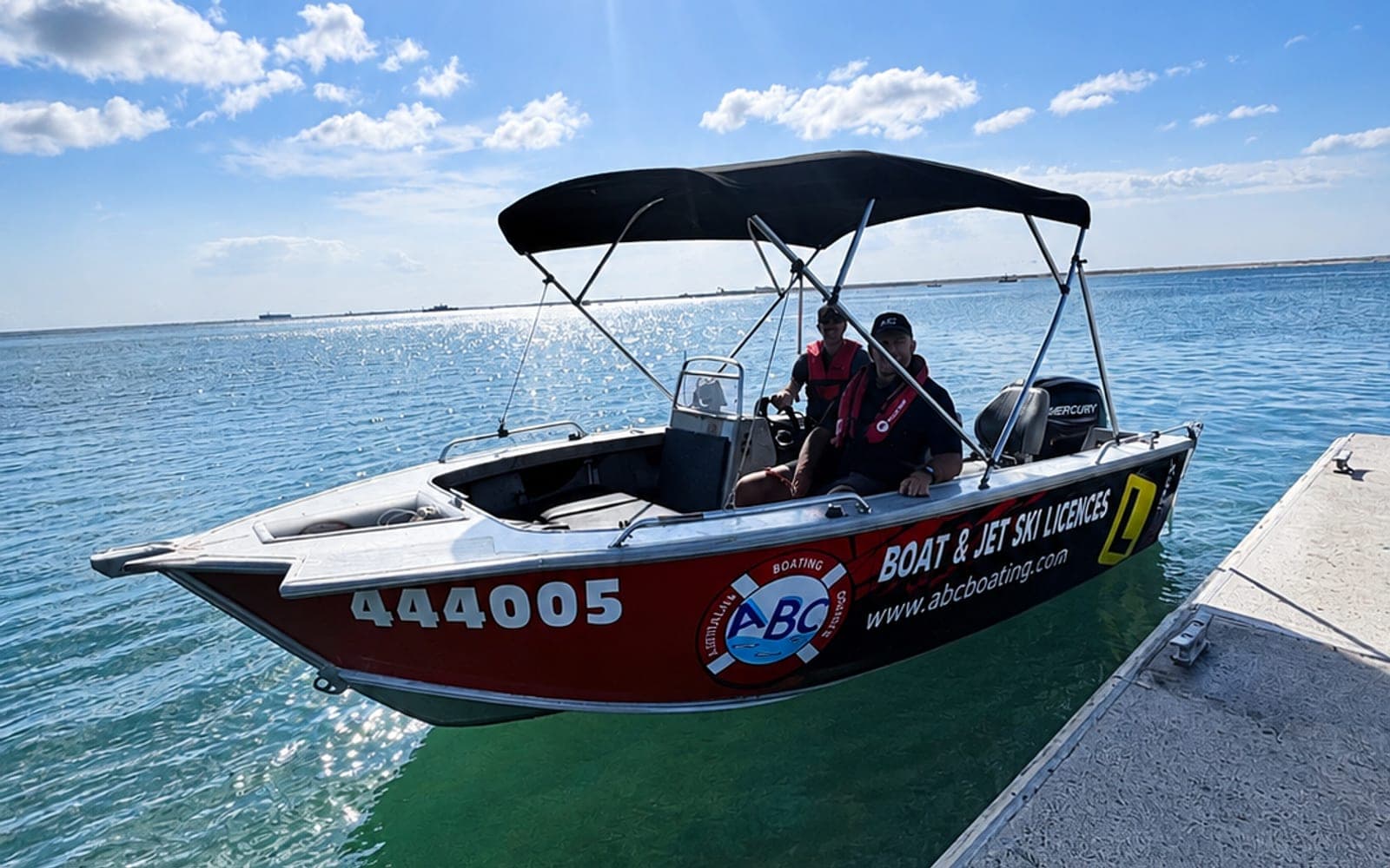 The ABC Boating training boat on the water off Caloundra with an instructor and student aboard, moored alongside a pontoon
