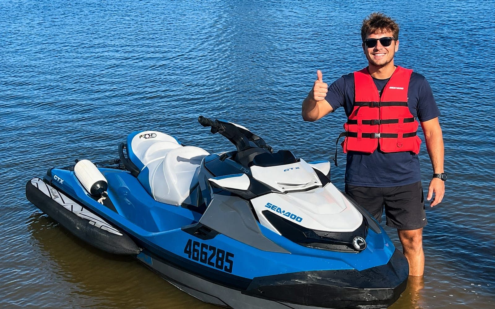 A student in a lifejacket giving a thumbs up beside a Sea-Doo jet ski in the shallows of the Maroochy River at Maroochydore