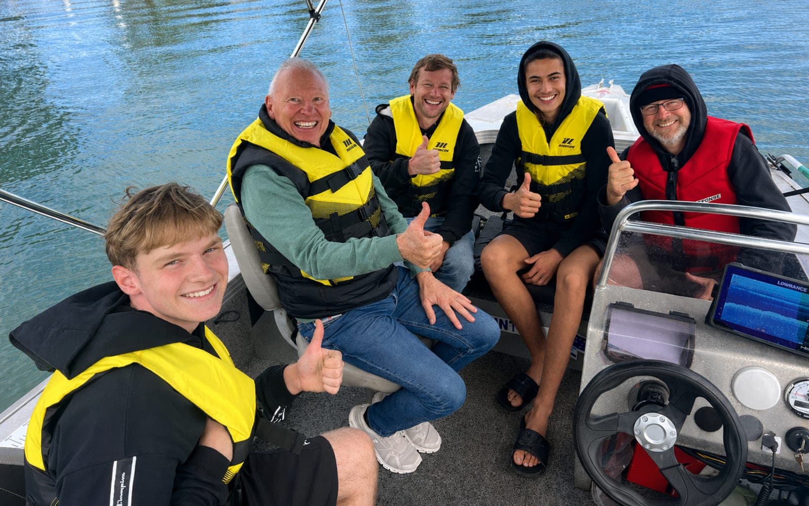 Five students in lifejackets aboard the ABC Boating training boat on the Noosa River, giving a thumbs up with the instructor at the helm